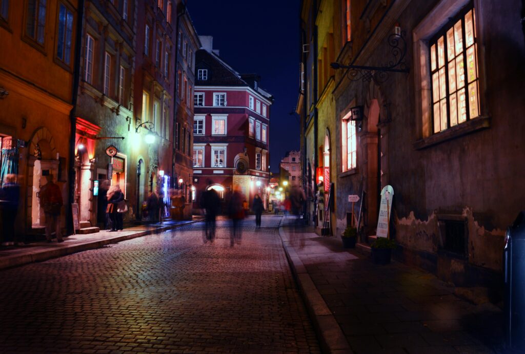 Charming night scene in a historic European city with blurred figures strolling under warm streetlights.